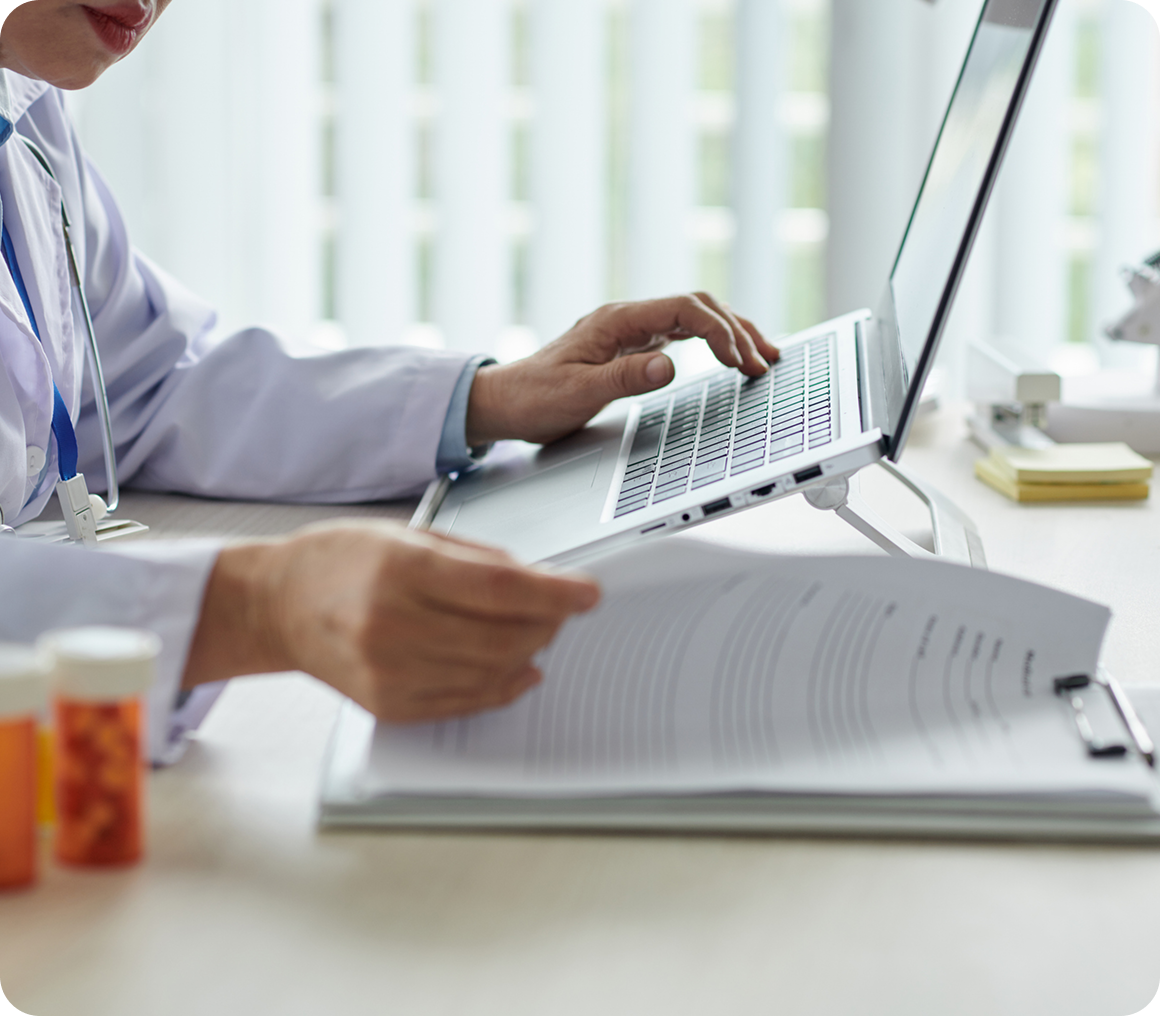 Physician examining paperwork and laptop